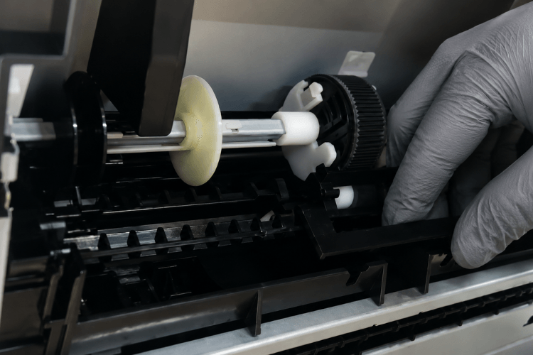 Technician inspecting worn pickup and feed rollers inside an HP LaserJet paper tray